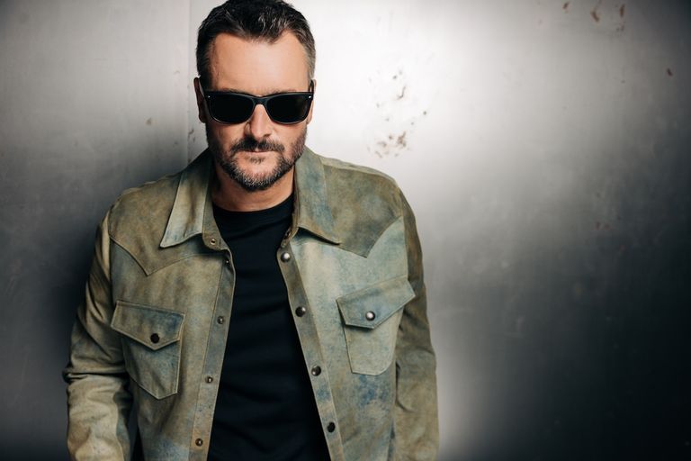 Country music singer Eric Church posing in sunglasses and a distressed leather jacket against a metallic background.